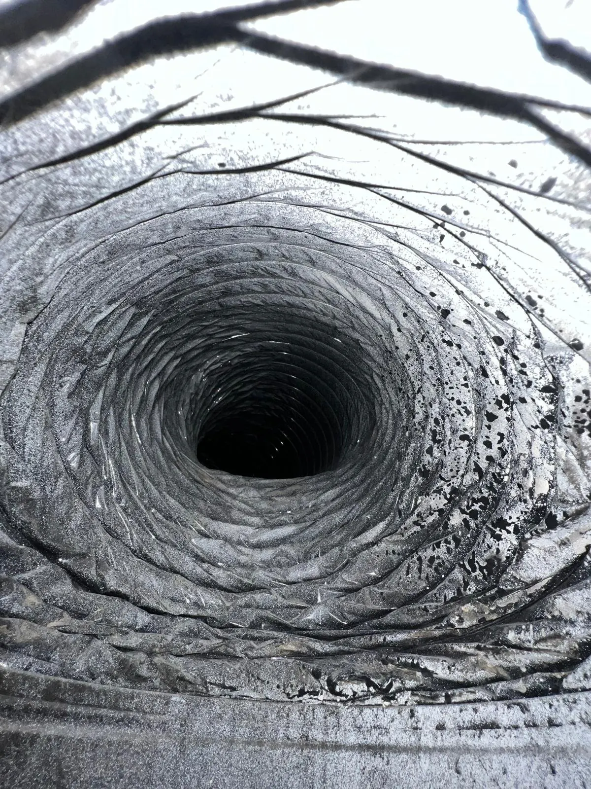Inside view of a dirty flexible air duct with heavy black dust and debris buildup before cleaning