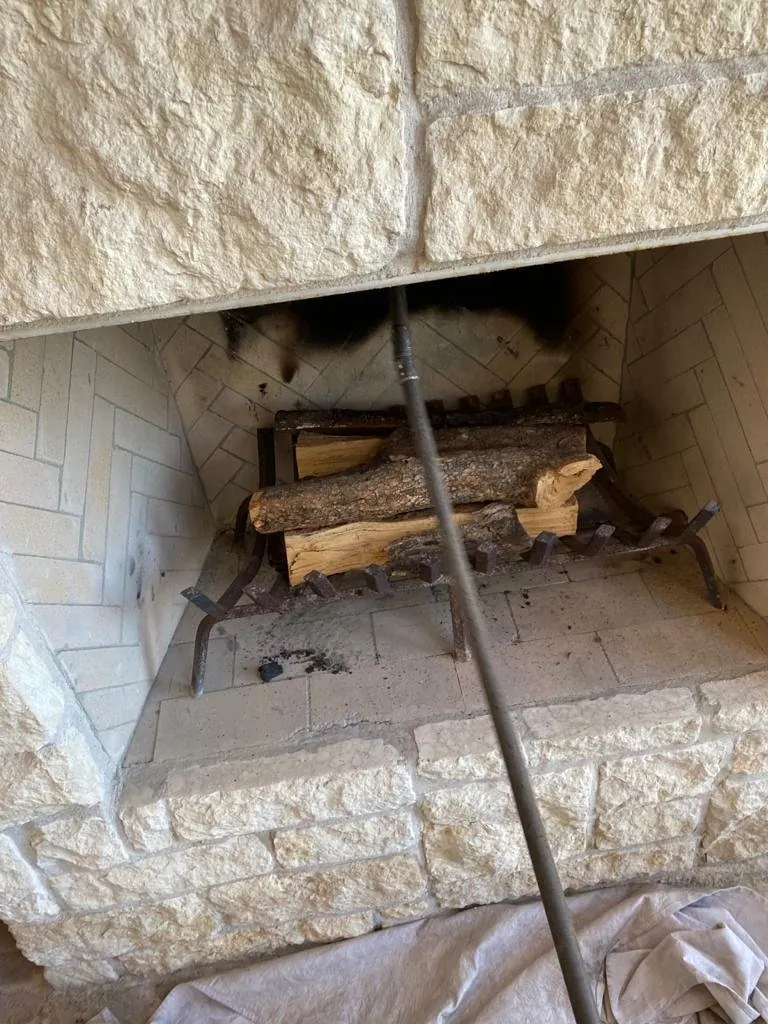 Chimney sweep in progress at a stone fireplace, with a cleaning rod pushed up the flue and a drop cloth protecting the floor