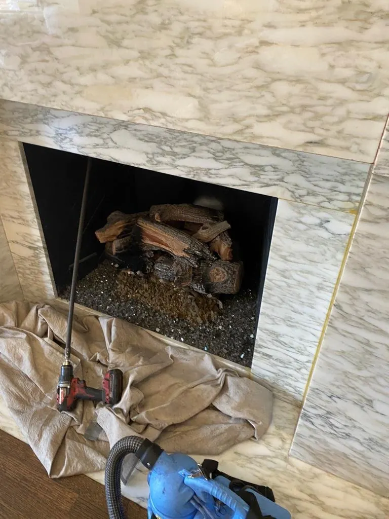 Chimney sweep setup at a marble fireplace with a drop cloth, drill-driven cleaning rod and vacuum ready to clean the flue