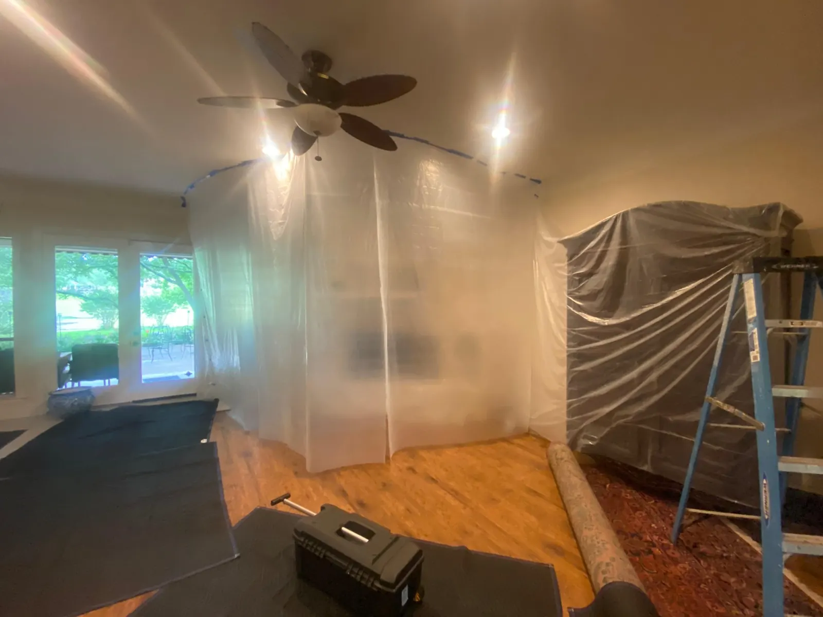 Living room prepped for a chimney sweep, with plastic dust containment around the fireplace, floor blankets, wrapped furniture and a ladder