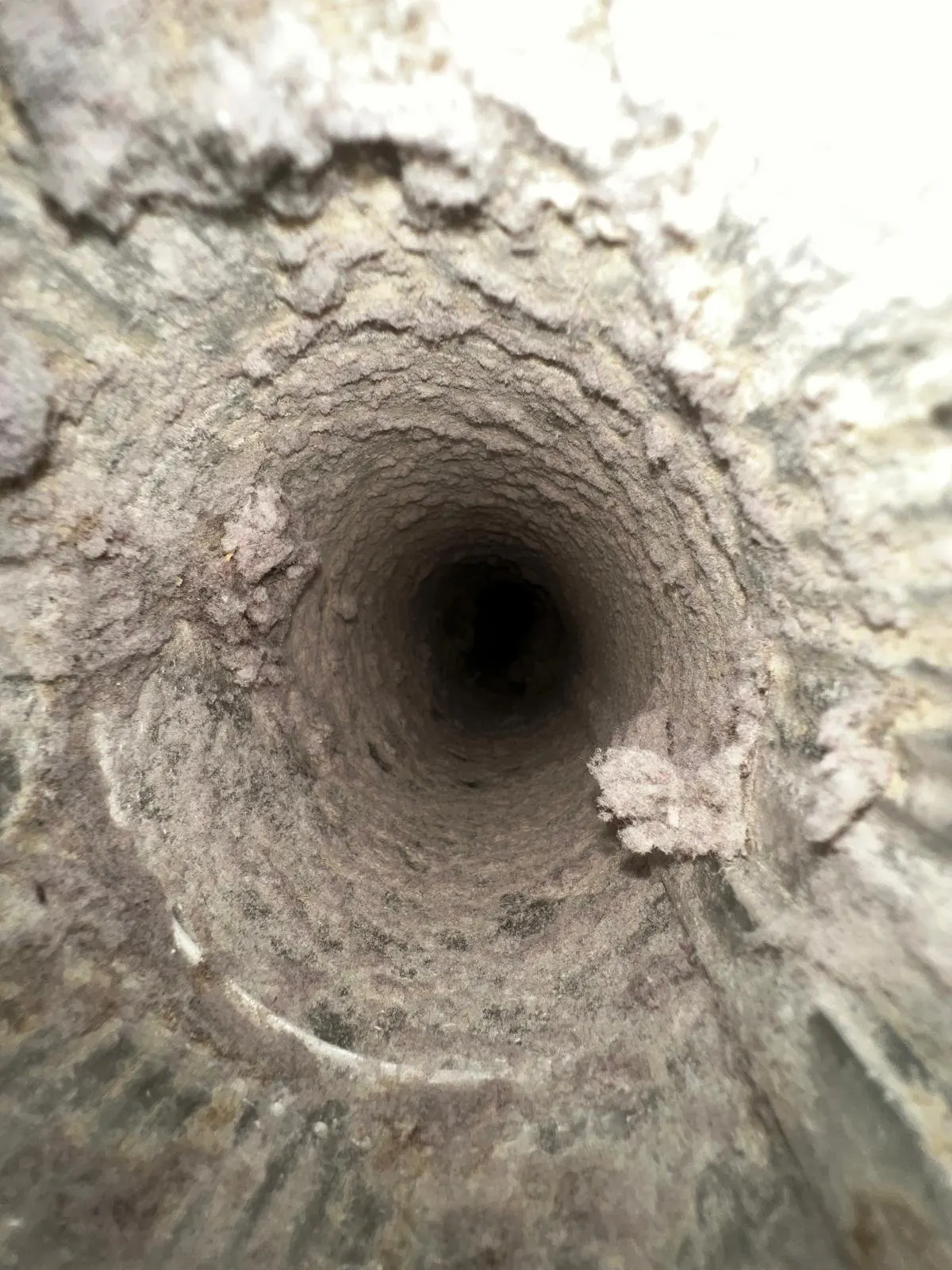 Inside of a clogged dryer vent duct with thick layers of lint built up along the walls, before cleaning