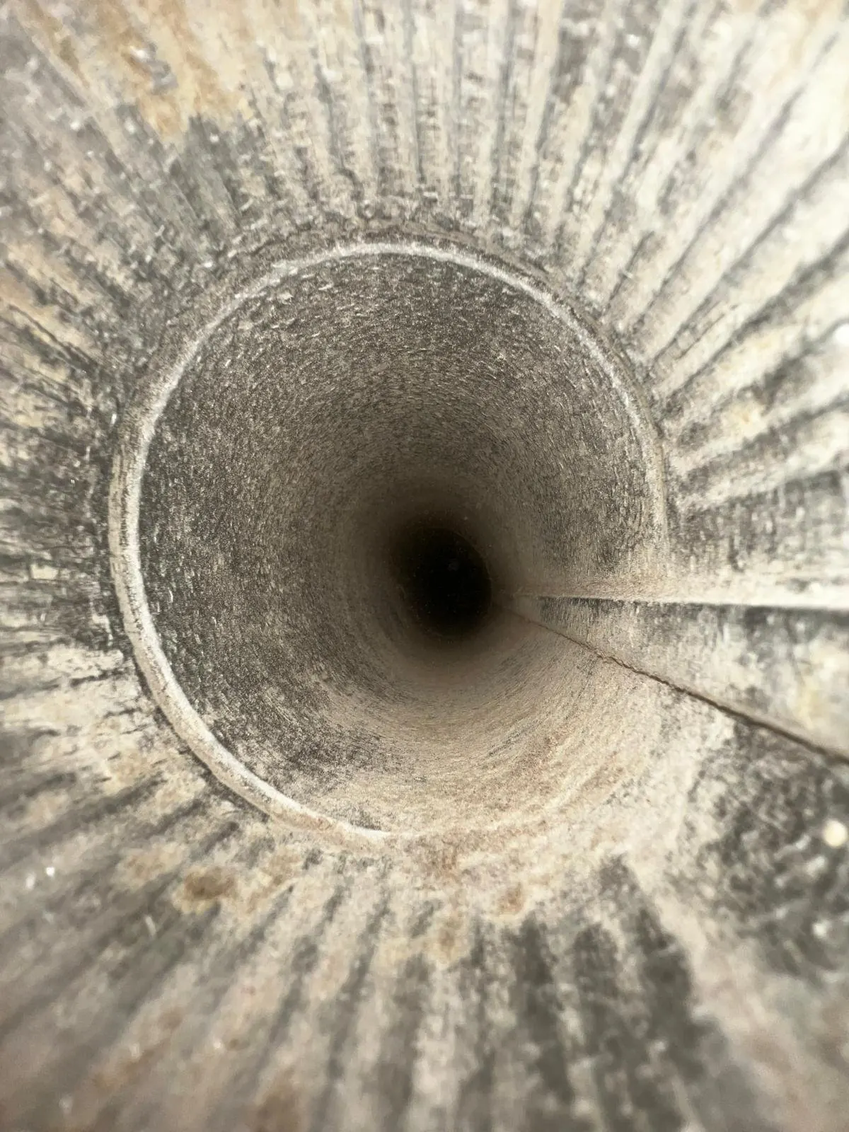 Looking down inside a dryer vent duct coated with dust and lint buildup before cleaning