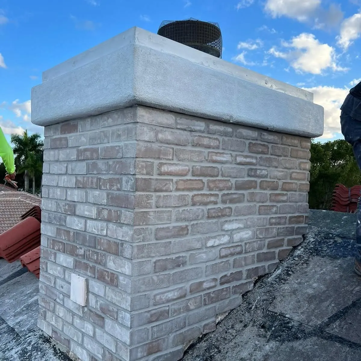Freshly rebuilt brick chimney with a new concrete crown and mesh-covered cap on a tile roof